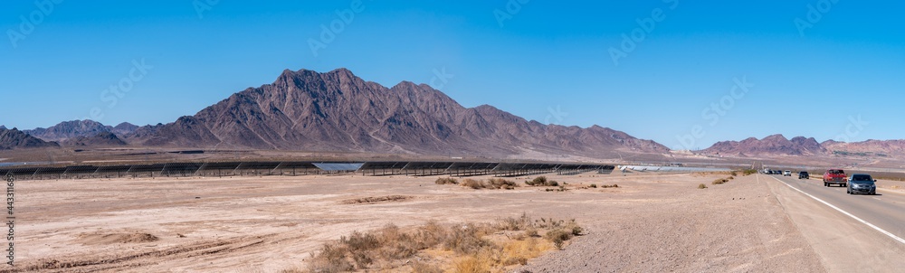 Panoramic View of Highway With Large Solar Farm on the Side of the Road and Large Mountains Formation on the background