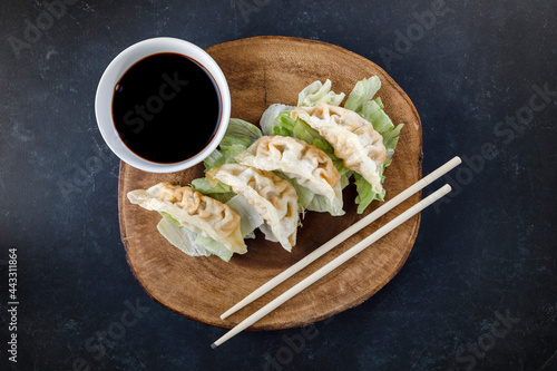 Gyozas served in black plate on wooden log, with chopsticks and black background