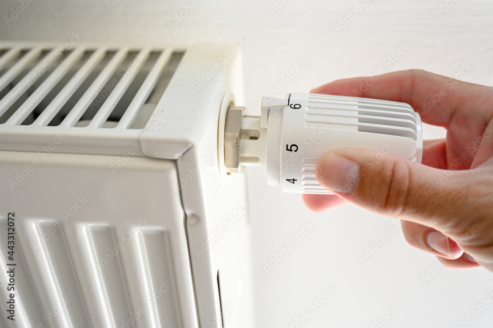 Hand adjusting the temperature on valve of a radiator at home. Close up of Man's hand on thermostatic valve in apartment. Adjusting radiator temperature in room at winter. Hand adjusting the temperature on valve of a radiator at home. Close up of Man's hand on thermostatic valve in apartment. Adjusting radiator temperature in room at winter.