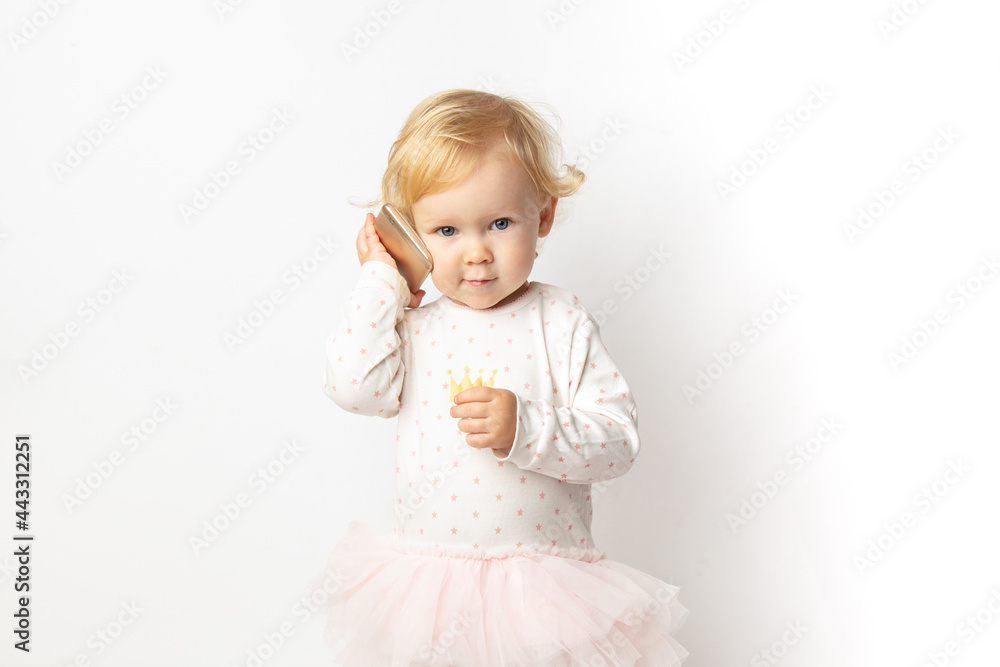funny angry curly caucasian baby girl with a mobile phone in her hands with a serious face on a white background with copy space. concept bad cellular connection. funny angry curly caucasian baby girl with a mobile phone in her hands with a serious face on a white background with copy space. concept bad cellular connection.