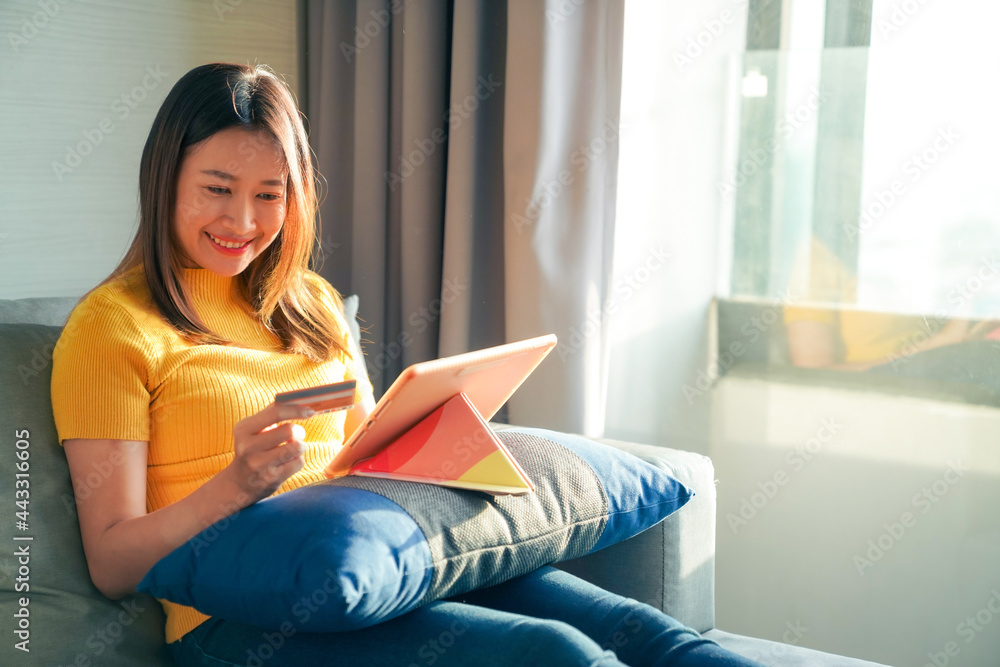Asian woman sitting on sofa using digital tablet with credit card for online shopping. Female shopper enjoy purchase goods in online store with e-banking online payment on mobile application at home. Asian woman sitting on sofa using digital tablet with credit card for online shopping. Female shopper enjoy purchase goods in online store with e-banking online payment on mobile application at home.