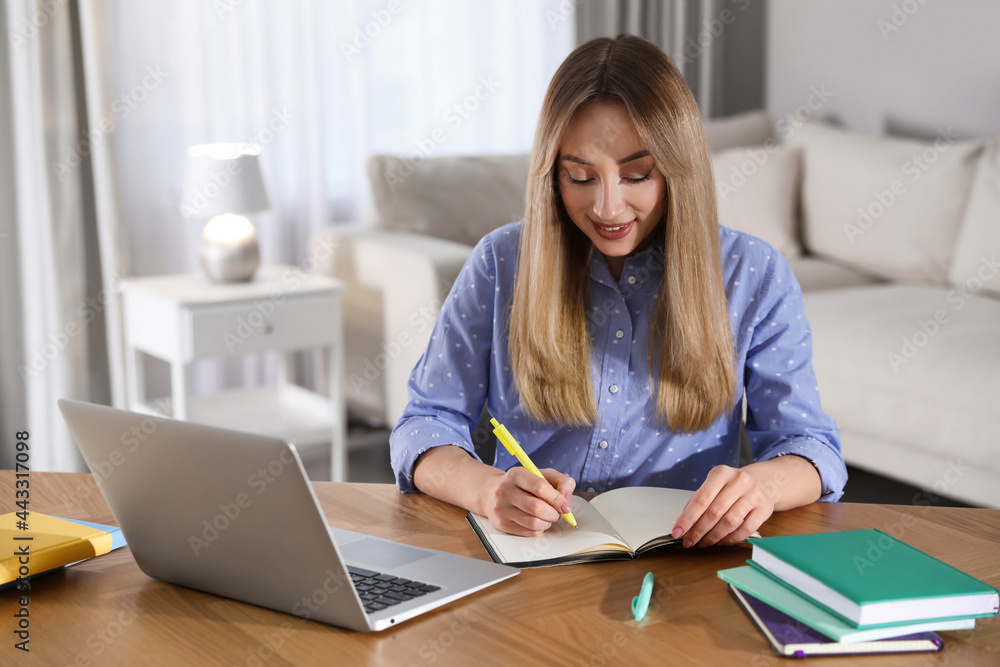 Young woman writing down notes during webinar at table in room Young woman writing down notes during webinar at table in room