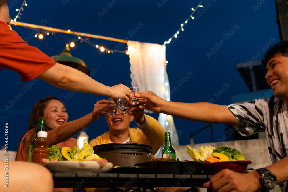 Group of Asian millennial people friends toasting alcoholic drink shot glasses while having outdoor dinner party with eat barbecue grill at rooftop for meeting reunion and holiday celebration together - obrazy, fototapety, plakaty 