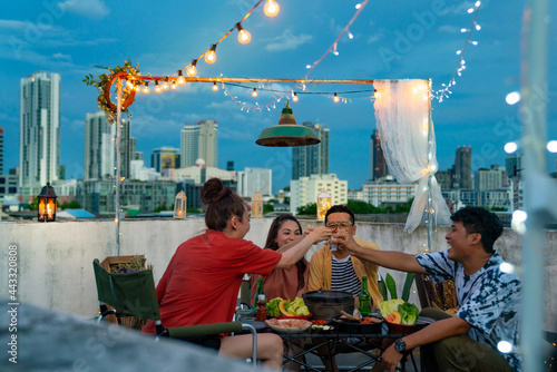 Group of Asian millennial people friends toasting alcoholic drink shot glasses while having outdoor dinner party with eat barbecue grill at rooftop for meeting reunion and holiday celebration together