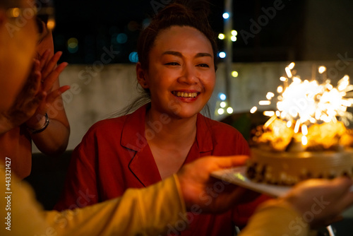 Diversity Asian millennial people friends enjoy celebration birthday party together at outdoor rooftop with food and drink. Woman excited with birthday cake and blowing birthday candle with happiness