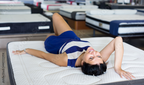 cheerful customer girl is lying testing new mattress before buying it in mattress shop