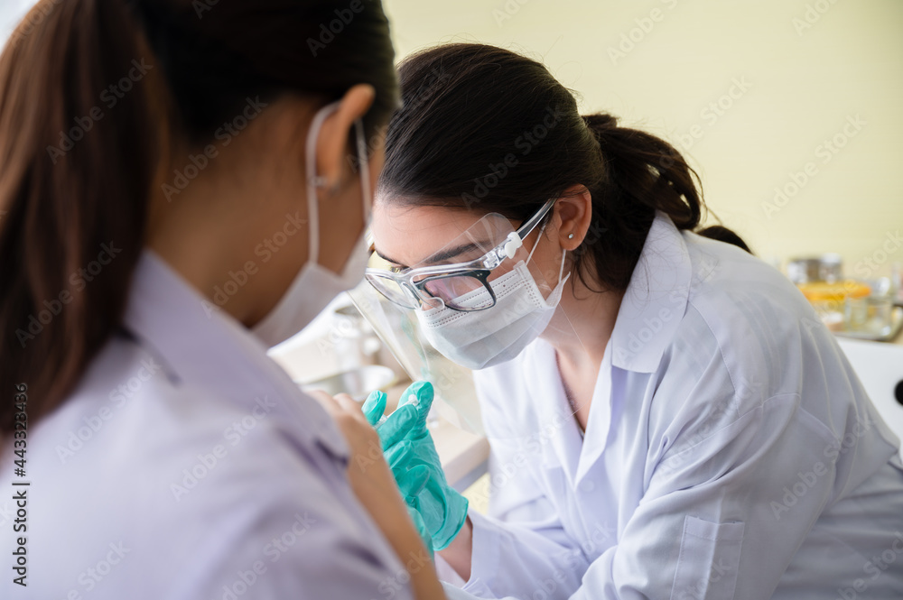 A female doctor or nurse wearing a mask, glove, and face shield are injecting the coronavirus 19 vaccine on the shoulder of the woman to immunize. Concept of preventing the spread of COVID-19. A female doctor or nurse wearing a mask, glove, and face shield are injecting the coronavirus 19 vaccine on the shoulder of the woman to immunize. Concept of preventing the spread of COVID-19.