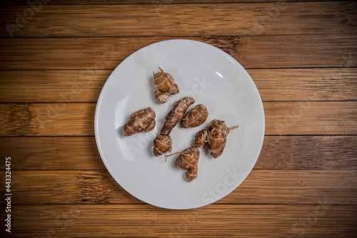 Jerusalem artichoke tubers on white plate, wood background, ingredient seasoning herb vegetable