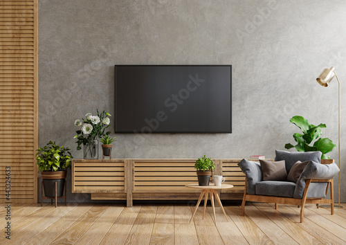 Mock up cabinet tv wall mounted in a cement room with armchair and table.