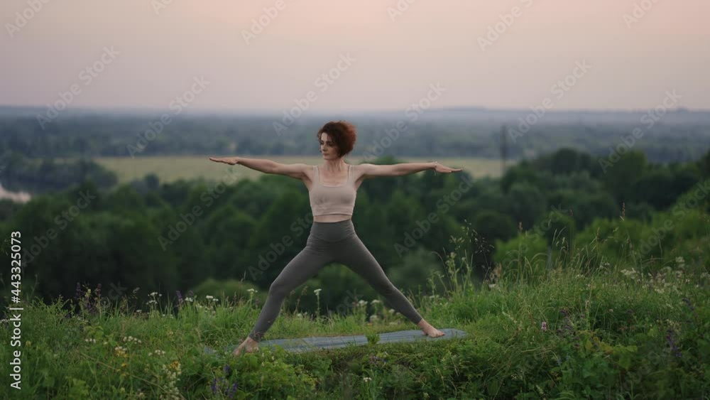 A young woman does yoga exercises standing on the top of a forest mountain against the background of a river and a forest landscape. Balance of body and spirit, relaxation and meditation A young woman does yoga exercises standing on the top of a forest mountain against the background of a river and a forest landscape. Balance of body and spirit, relaxation and meditation