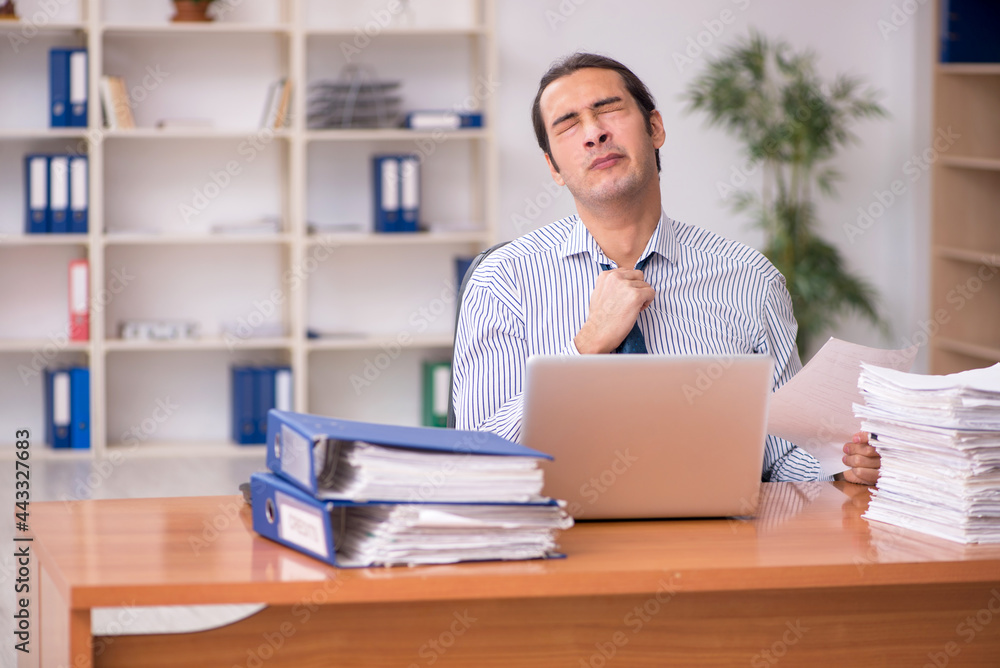 Young male employee unhappy with excessive work in the office Young male employee unhappy with excessive work in the office