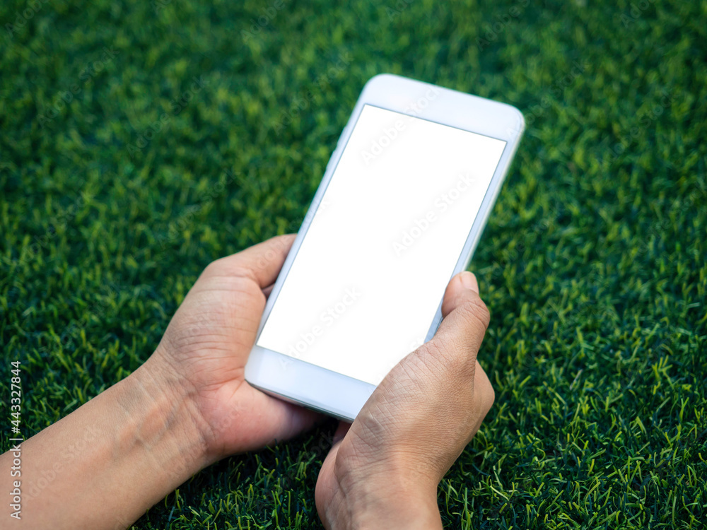 Mockup image of phone. Close-up white blank screen on mobile phone in hands on green artificial grass background. Hand holding white smartphone with empty screen.
