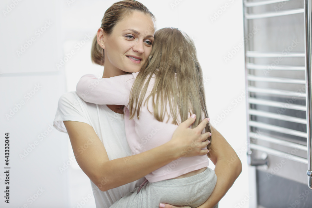Young woman holding little daughter in her arms and hugging tightly at home Young woman holding little daughter in her arms and hugging tightly at home