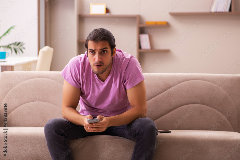 Obraz premium Young man watching tv at home during pandemic