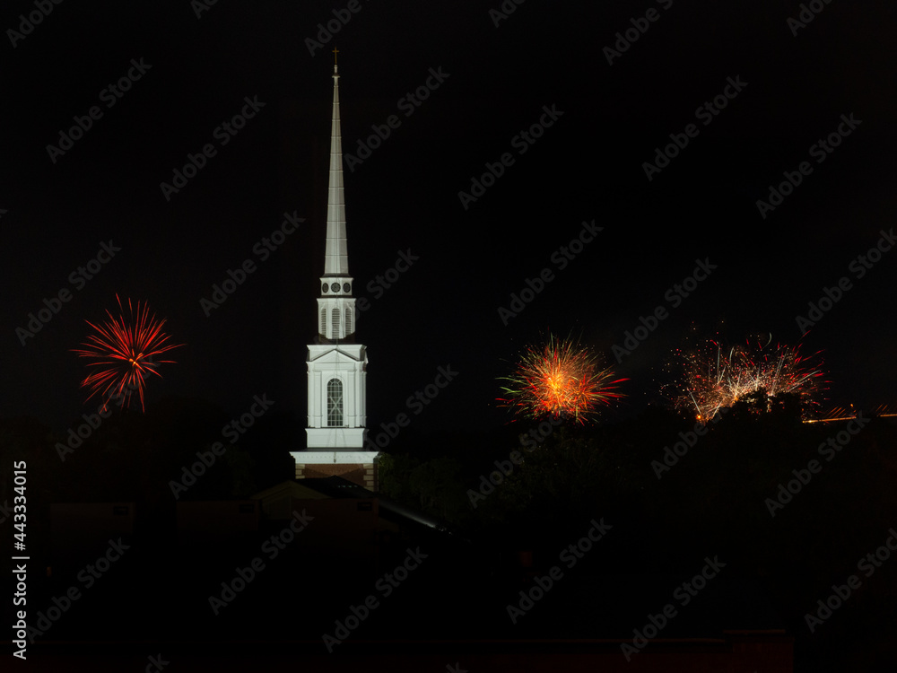 Fireworks exploding in the sky behind a church steeple