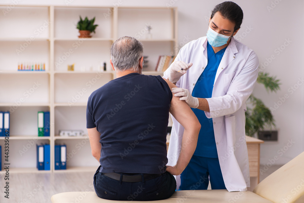 Fototapeta premium Old man visiting young doctor in covid-19 vaccination concept