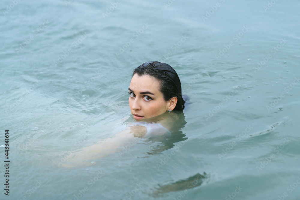 A dark-haired girl swims in the lake and takes a photo session