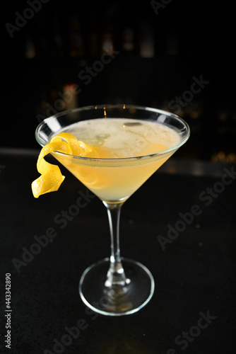 iced yellow lemon fruit juice cocktail or mocktail with lemon peel in glass goblet on black marble bar counter dark night background cold alcohol drink menu