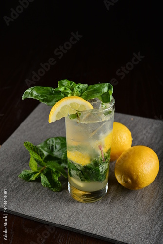 iced basil lemon mint leaf cooler mocktail / kombucha in glass on bar counter dark night background cold halal drink menu