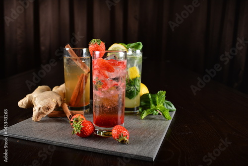 iced cooler juice colourful mocktail drink with ginger, strawberry, lemon kombucha in glass on bar counter dark night background cold halal drink menu