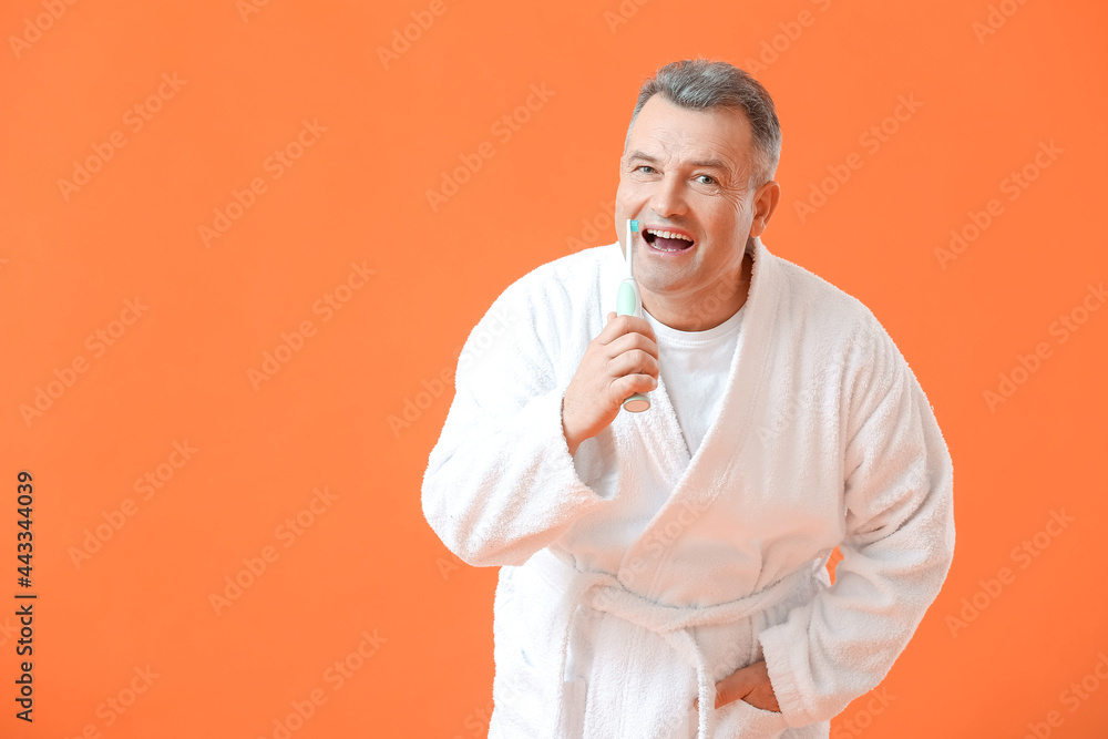 Mature man brushing teeth on color background