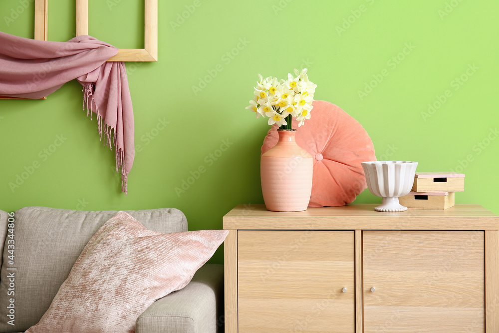 Vase with narcissus flowers on chest of drawers in room