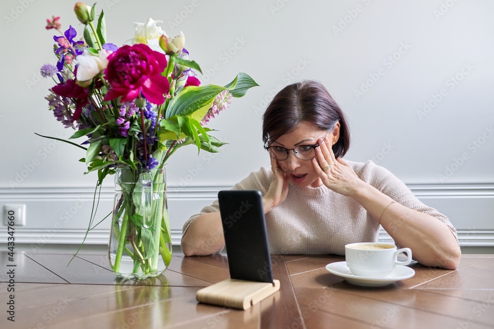 Surprised emotional mature woman looking at smartphone screen Surprised emotional mature woman looking at smartphone screen