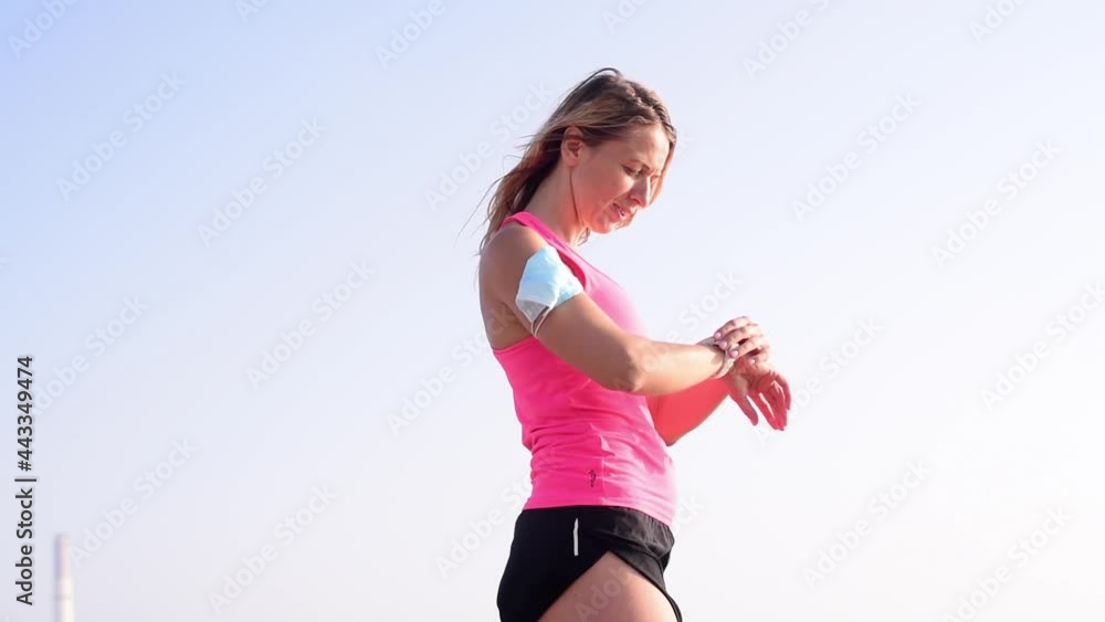 One blonde girl in pink top stay on beach, looks on smartwatch, goes in for sports with mask on arm. Get active and stay fit. Outdoors, on Sunset One blonde girl in pink top stay on beach, looks on smartwatch, goes in for sports with mask on arm. Get active and stay fit. Outdoors, on Sunset