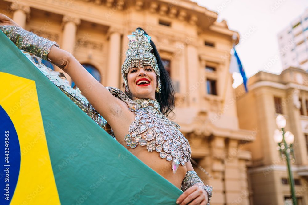 Beautiful Brazilian woman wearing colorful Carnival costume and Brazil flag during Carnaval street parade in city.