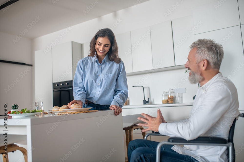 Obraz premium Young woman making breakfast, her handicapped husband sitting near