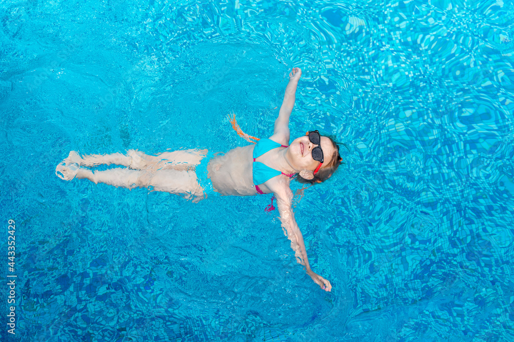 little girl in sunglasses lies on the water in the swimming pool and enjoys the sun and summer