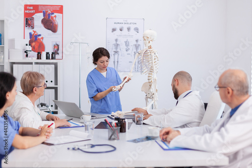 Hospital woman nurse presting bone structure using body anatomy skeleton discussing medical expertise. Physician team working in meeting room at healthcare treatment explaining health diagnosis