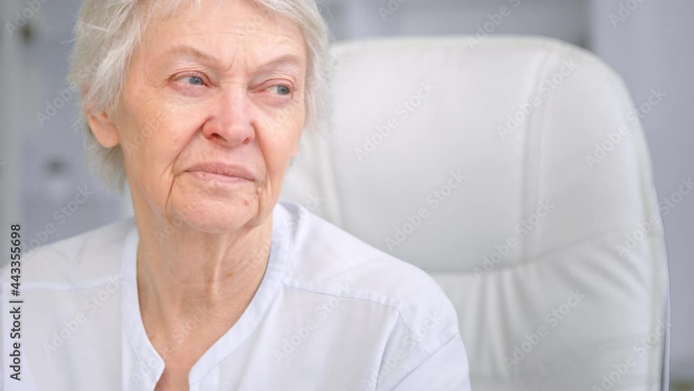 Old mother with wrinkly face and sad blue eyes looks aside