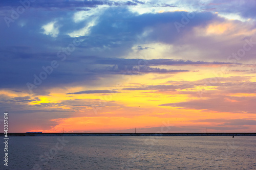 Beautiful sunset over sea coast. Multicolored blue-violet-orange-yellow sky with curly majestic clouds at sunset. Quiet water. A breakwater on the horizon. Travel vacation holiday relax time concept.