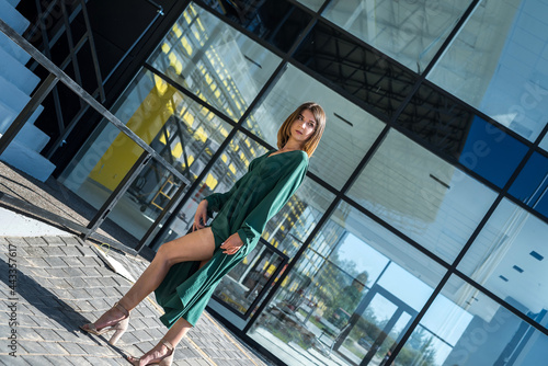 fashion and happy woman in green dress standing against modern glass architecture