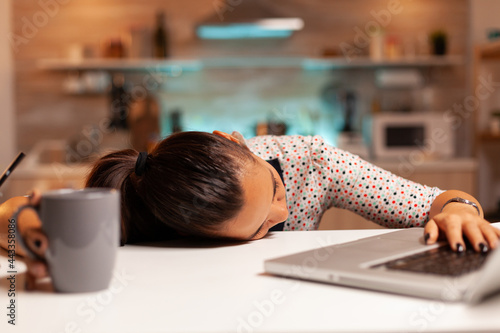 Freelance woman falling asleep in home kitchen working overtime on a project. Employee using modern technology at midnight doing overtime for job, business, busy, career, network, lifestyle ,wireless.