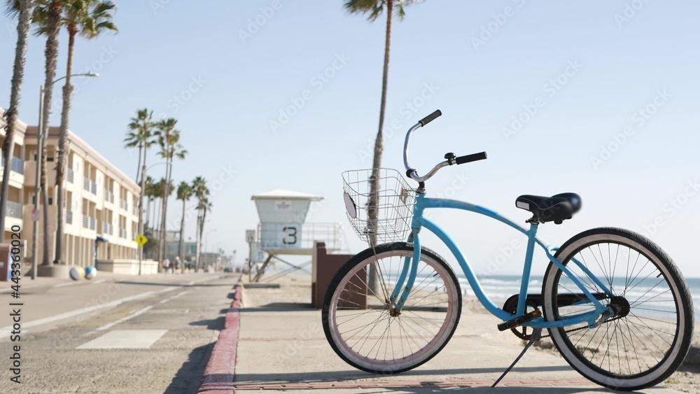 Blue bicycle, cruiser bike by sandy ocean beach, pacific coast near Oceanside pier, California USA. Summertime vacations, sea shore. Vintage cycle, tropical palm trees, lifeguard tower watchtower hut