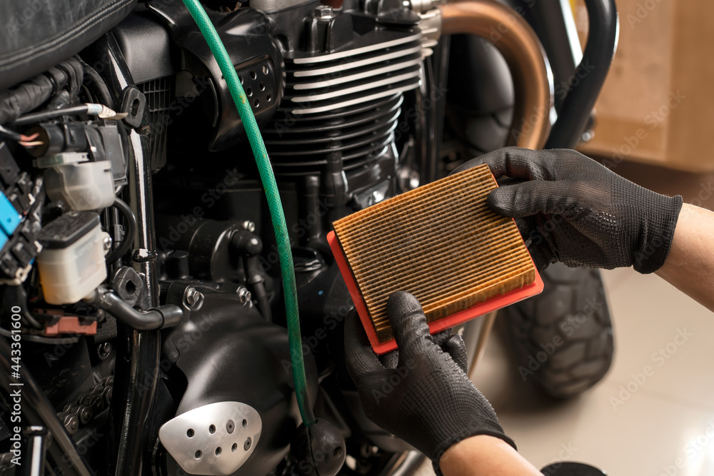 mechanic holding dirty Engine Air Filter over motorcycle, working in