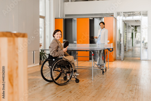 White woman in wheelchair playing ping-pong with her colleague