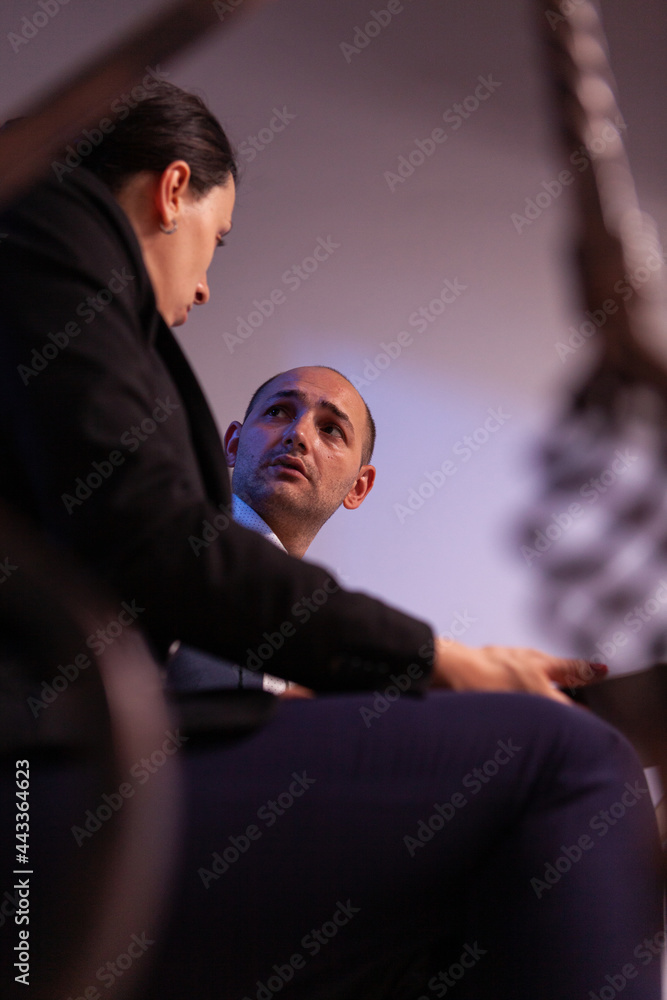 Stressed tired businesswoman working to finish project deadline with help from businesswoman. Colleague entrepreneur working late together in evening at corporate job sitting on staircase, explaining