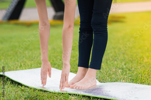 A woman training in the summer on the grass on the mat. Stretching the leg, touching the toe
