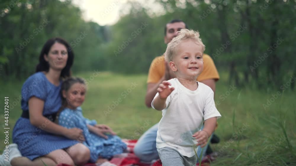 Happy family. Baby play with his parents in forest park. Family picnic on green grass in park. Baby run on green grass in forest. Happy family concept. People on picnic in park. Happy baby run Happy family. Baby play with his parents in forest park. Family picnic on green grass in park. Baby run on green grass in forest. Happy family concept. People on picnic in park. Happy baby run