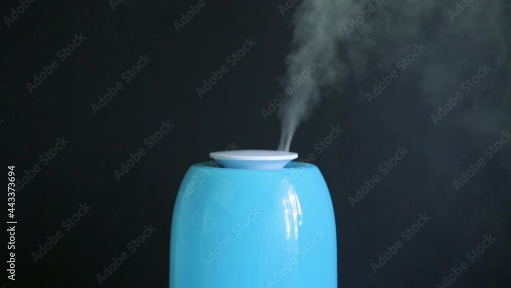 A blue ultrasonic humidifier works by releasing water vapor against a black background. A blue ultrasonic humidifier works by releasing water vapor against a black background.
