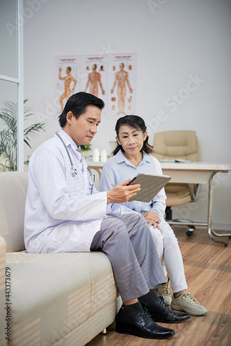Physician filling medical history on tablet computer when elderly woman talking about disease symptoms