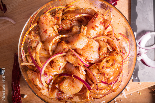 Fotografia Sliced pieces of chicken breast in a bowl marinated in hot spices and ingredients for preparing an oriental chicken dish on a cutting board with a Chinese knife