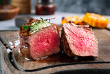 A large grilled filet Mignon steak with butter and thyme is served chopped on a wooden board. A dish of fried meat in close-up