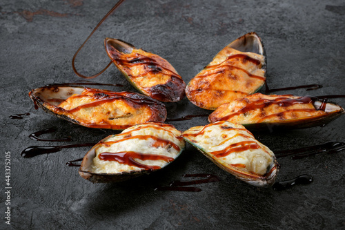 Shellfish mussels Baked with cheese in a shell on a black stone. Grilled mussels with teriyaki sauce.