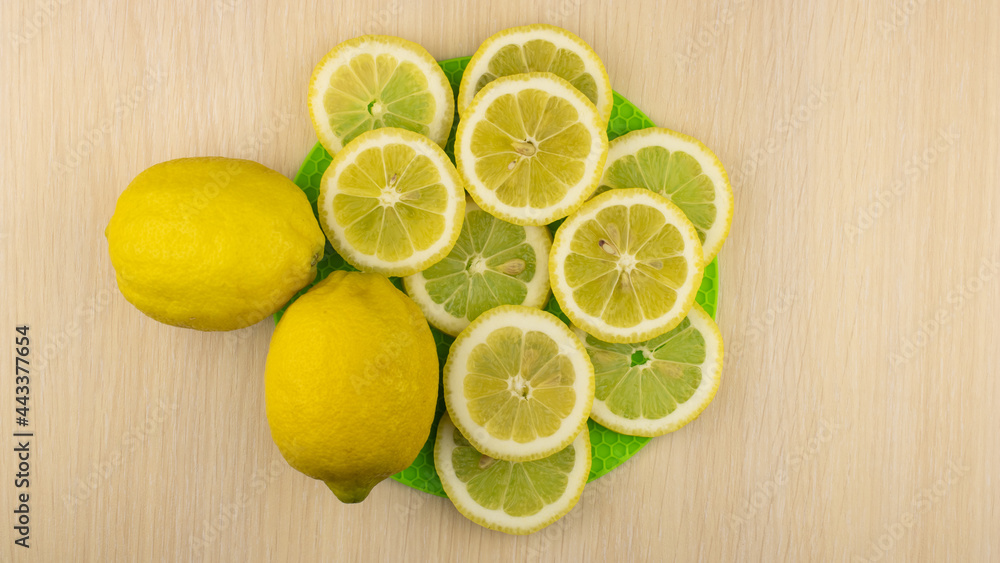The lemon slices are laid out on a green stand. Two whole lemons next to each other. Top view. The lemon slices are laid out on a green stand. Two whole lemons next to each other. Top view.