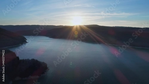 Aerial forward flight over blue calm Lac de Vouglans Lake during epic sunset behind mountain silhouette in France. photo