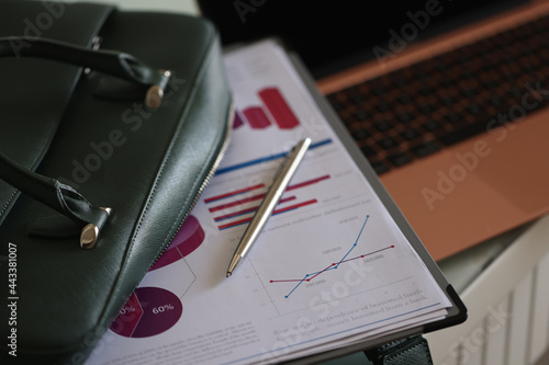 Clipboard documents and ballpoint pen lying on open green laptop bag closeup